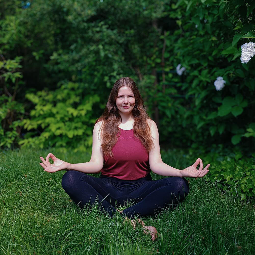Gründerin Sarah sitzend im Rasen in Yoga-Position.